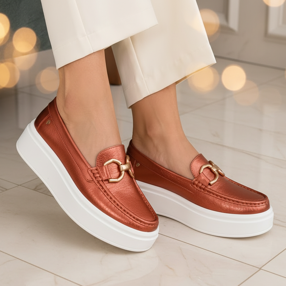 Women's metallic coral genuine leather platform loafers with gold-tone horsebit hardware and a white platform sole, styled with modern ivory trousers for a quiet luxury look.