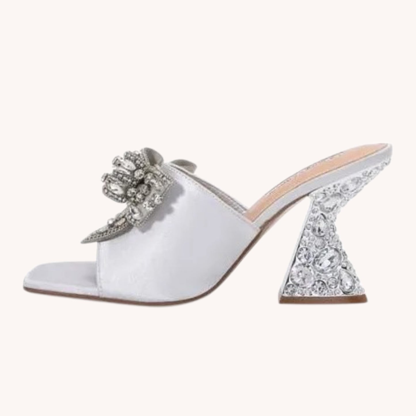 A single white satin mule sandal with a chunky high heel covered in clear rhinestones, featuring a matching rhinestone-embellished bow on the strap, shown against a solid off-white background.